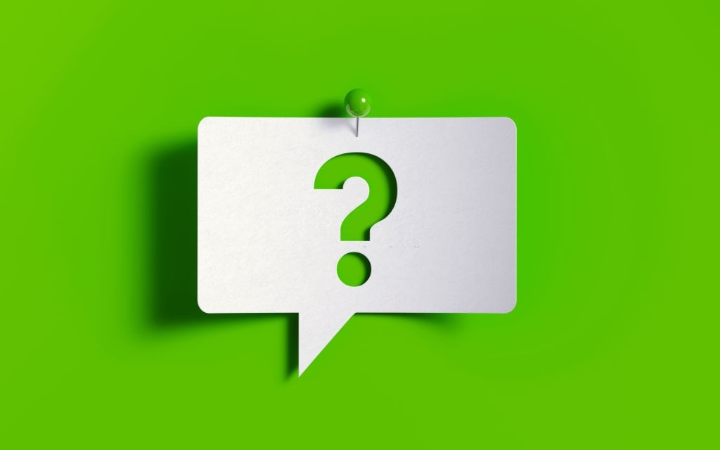 White post it note pinned with a green push pin on green background. There is a question mark symbol on the speech bubble. Horizontal composition with copy space.